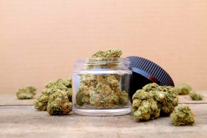 glass jar filled with cannabis flower buds, surrounded by loose nugs on a rustic wooden surface