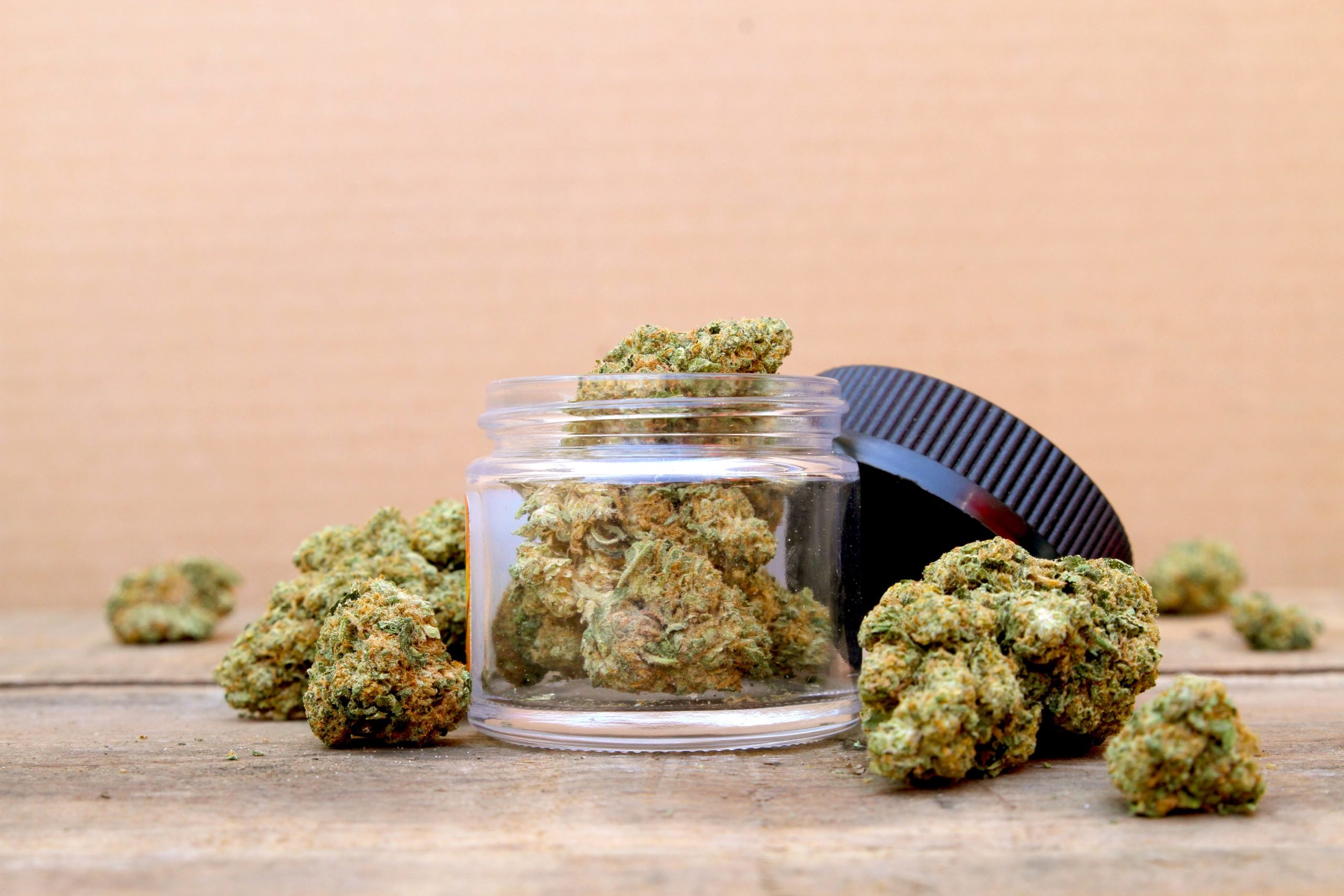 glass jar filled with cannabis flower buds, surrounded by loose nugs on a rustic wooden surface